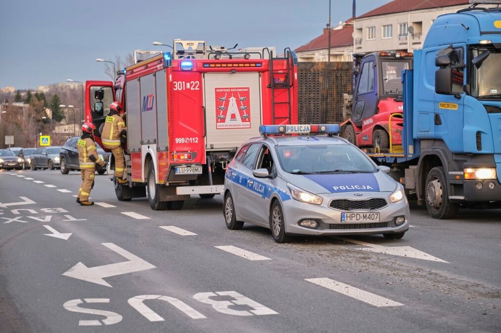 Ścieżka z betonu na ruchliwej ulicy. Policjanci wezwali na miejsce strażaków 1 radiowóz i wóz strażacki zabezpieczają pas jezdni