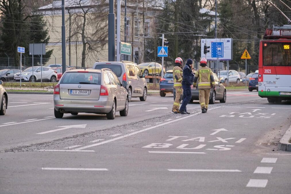 Ścieżka z betonu na ruchliwej ulicy. Policjanci wezwali na miejsce strażaków 3 Dwóch strażaków i policjant idą wzdłuż ścieżki z betonu na jezdni