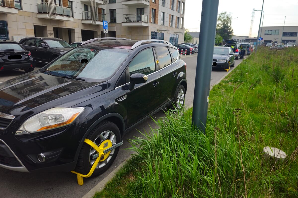 Strażnik miejski zakładający blokady na samochody na ul. Wojciechowskiej